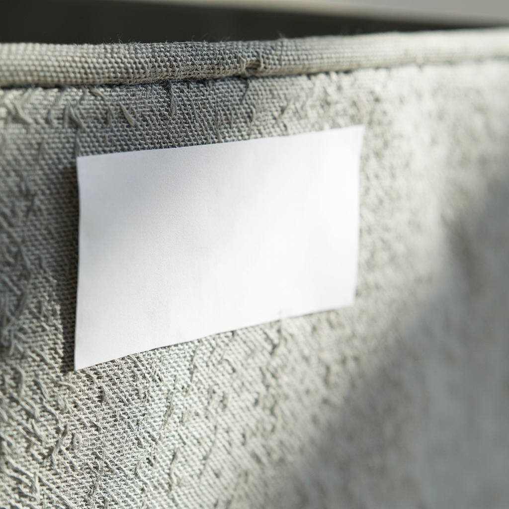 Close-up of a fabric storage bin with a removable white label showing season, initial, and date fields